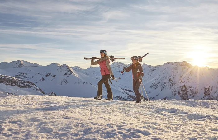 zwei Frauen mit Skiern auf den Schultern im Schnee